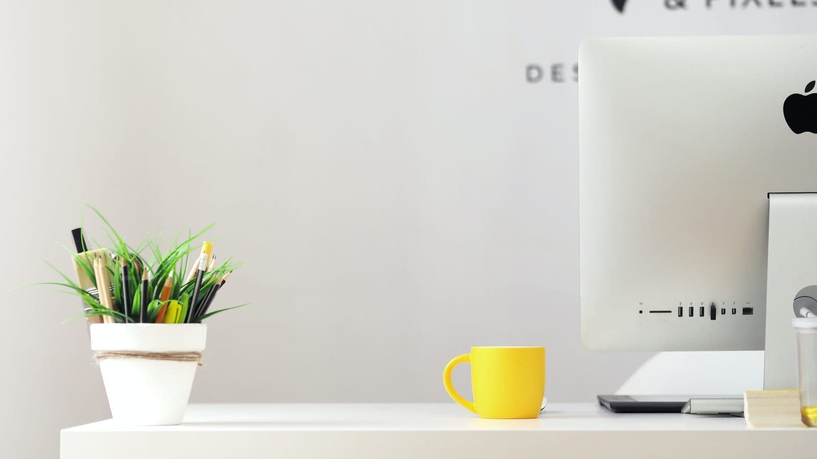An organised desk with plant, computer and coffee mug
